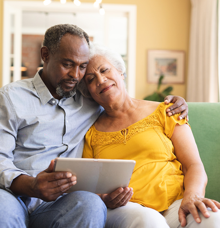 2 seniors with arms around each other while looking at computer tablet