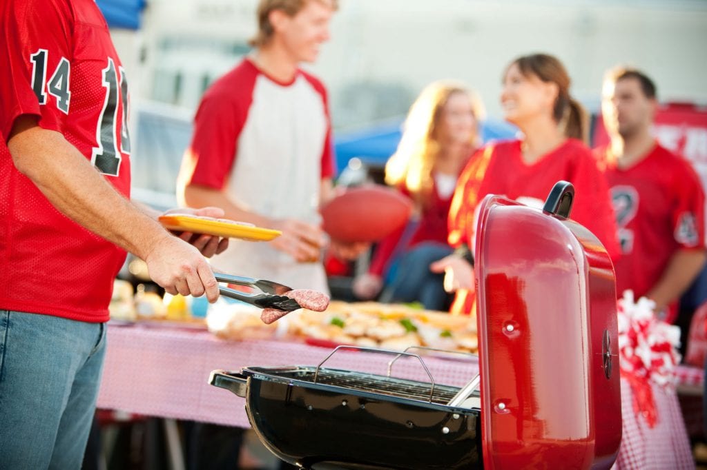 Extensive series of a multi-ethnic group of fans tailgating outside a stadium before a football game. Includes tickets, cooking, eating and fun.